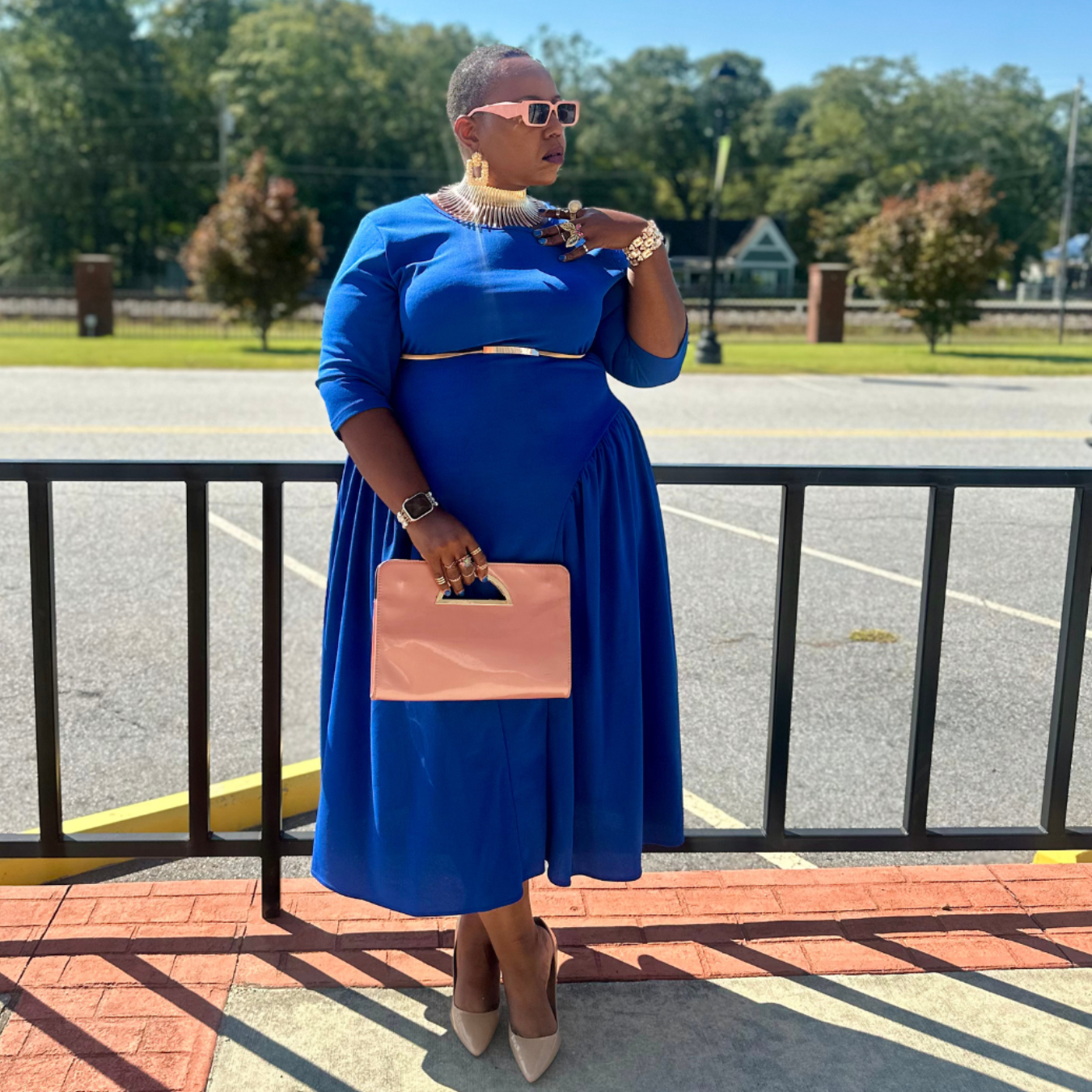 Woman in a blue dress holding a pink clutch in an outdoor setting.