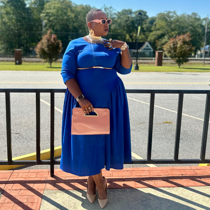 Woman in a blue dress holding a pink clutch in an outdoor setting.