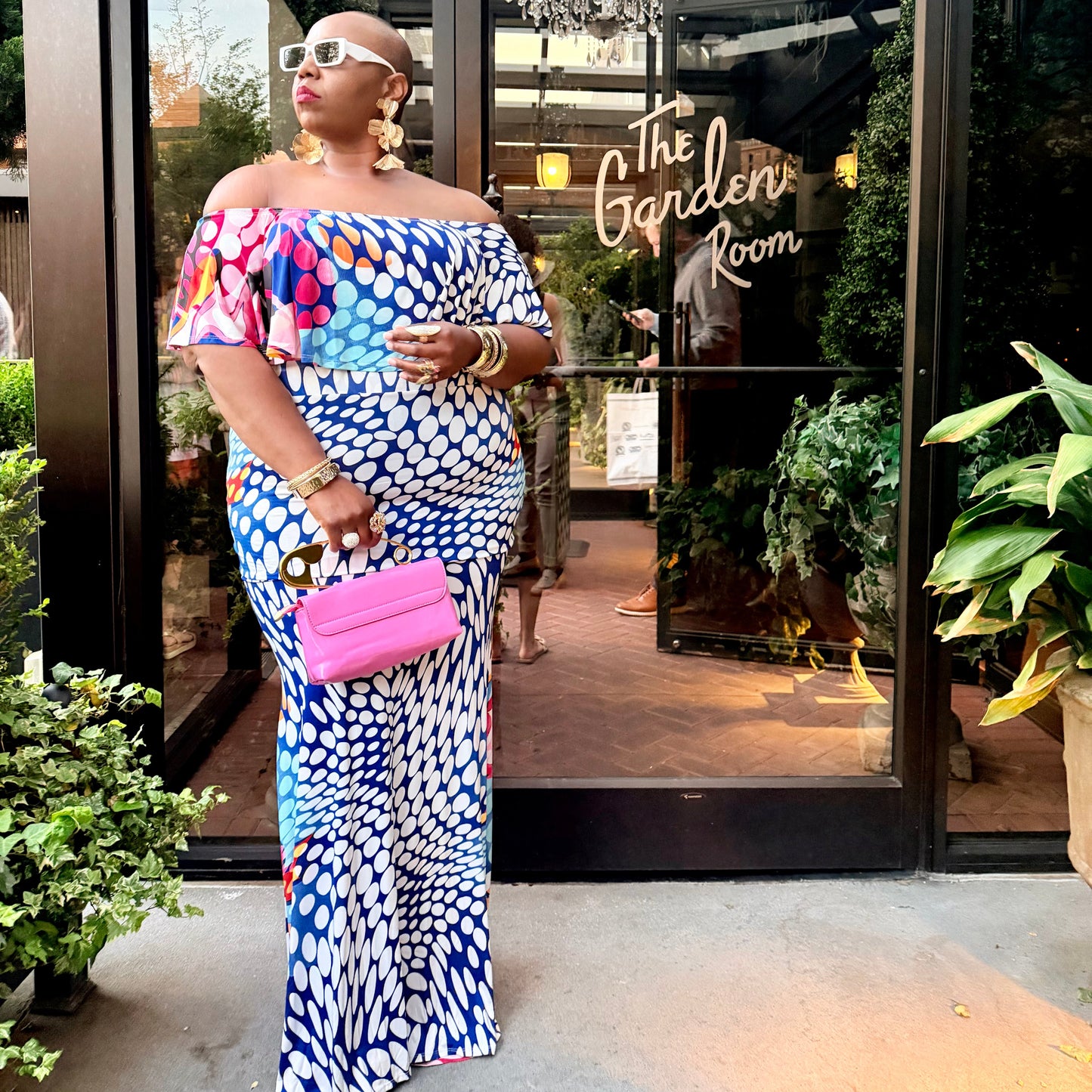 Woman in a colorful dress standing in front of 'The Garden Room' entrance.